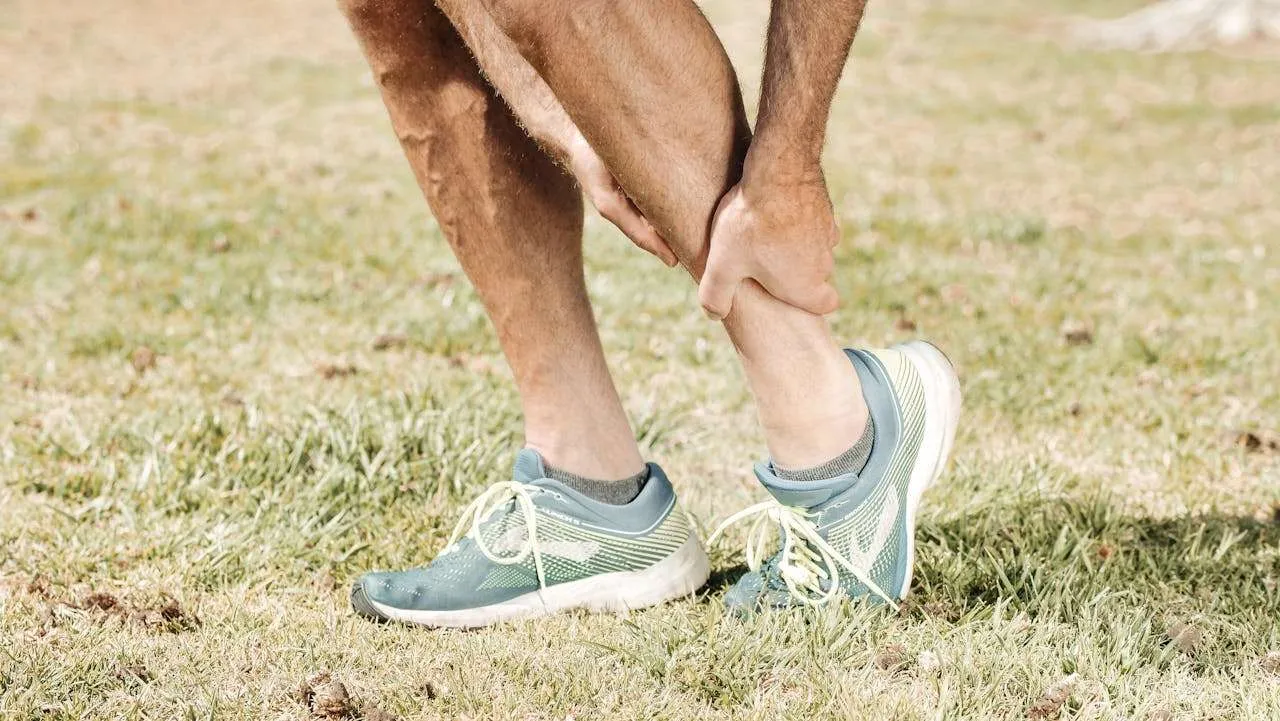 A man wearing running shoes on grass grabbing his leg in pain.