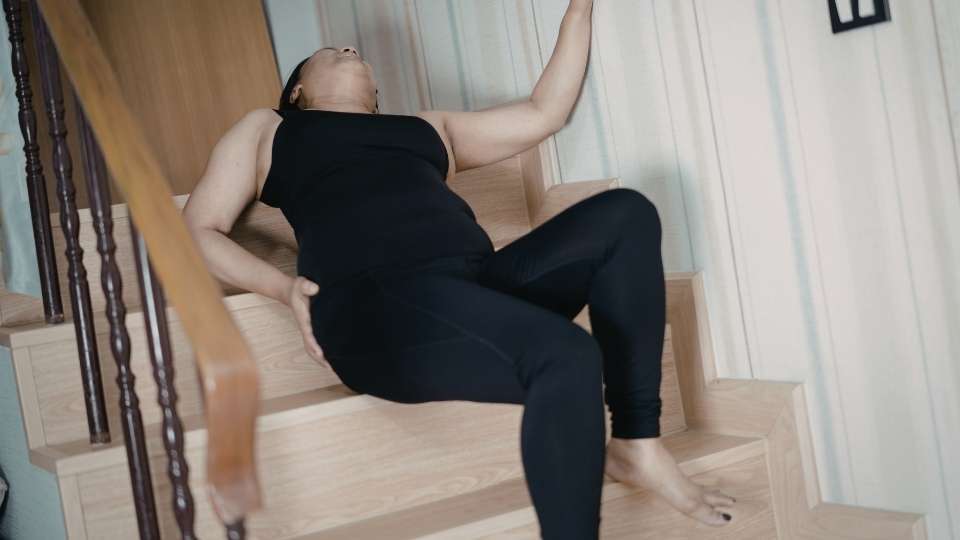 Woman falling backward on indoor stairs and reaching for the wall, illustrating a slip and fall injury at home