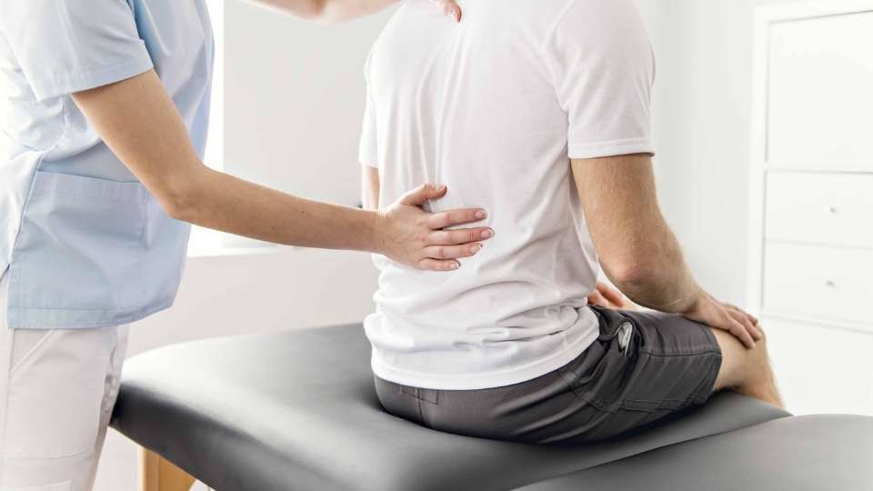 Healthcare professional performing a back examination on a patient sitting on a treatment table, assessing chronic back pain and spinal health