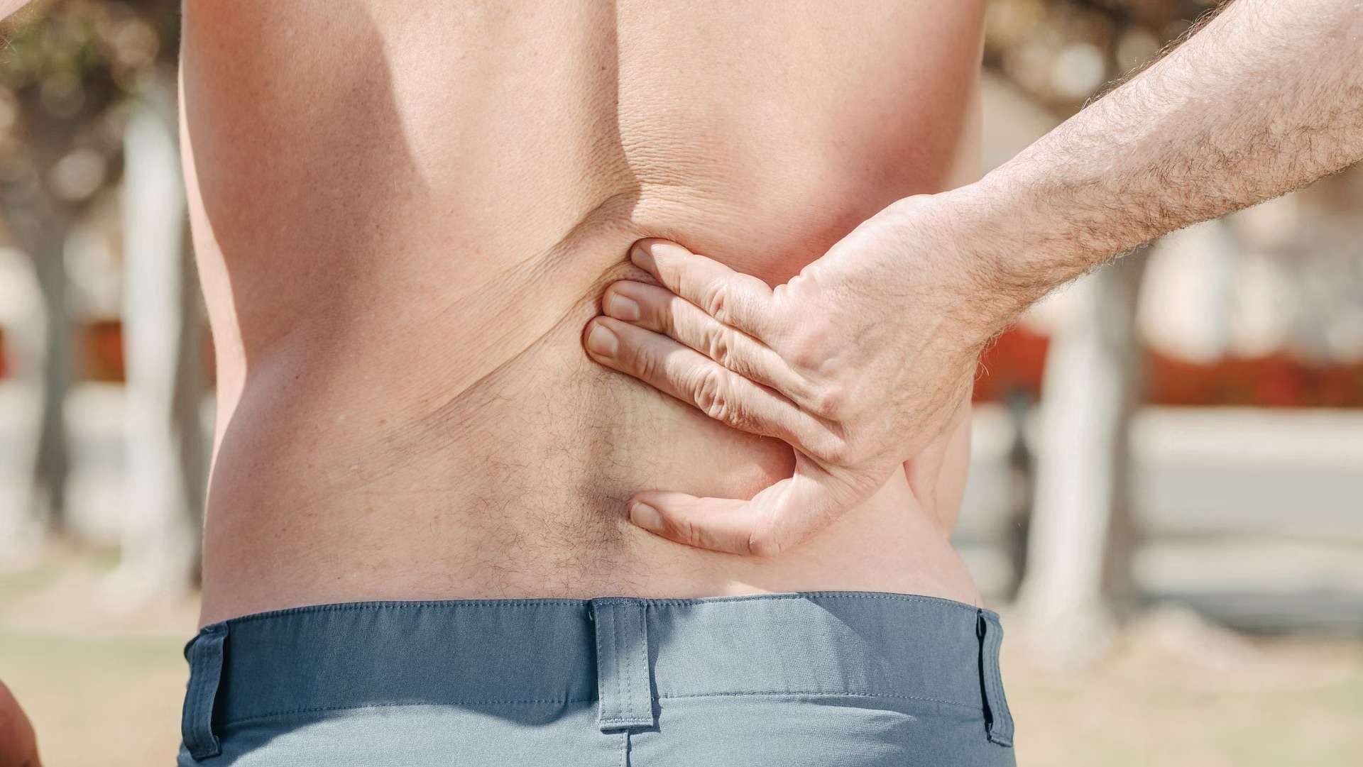 Adult holding their lower back with backbone pain, considering whether chiropractic care or medication offers better relief