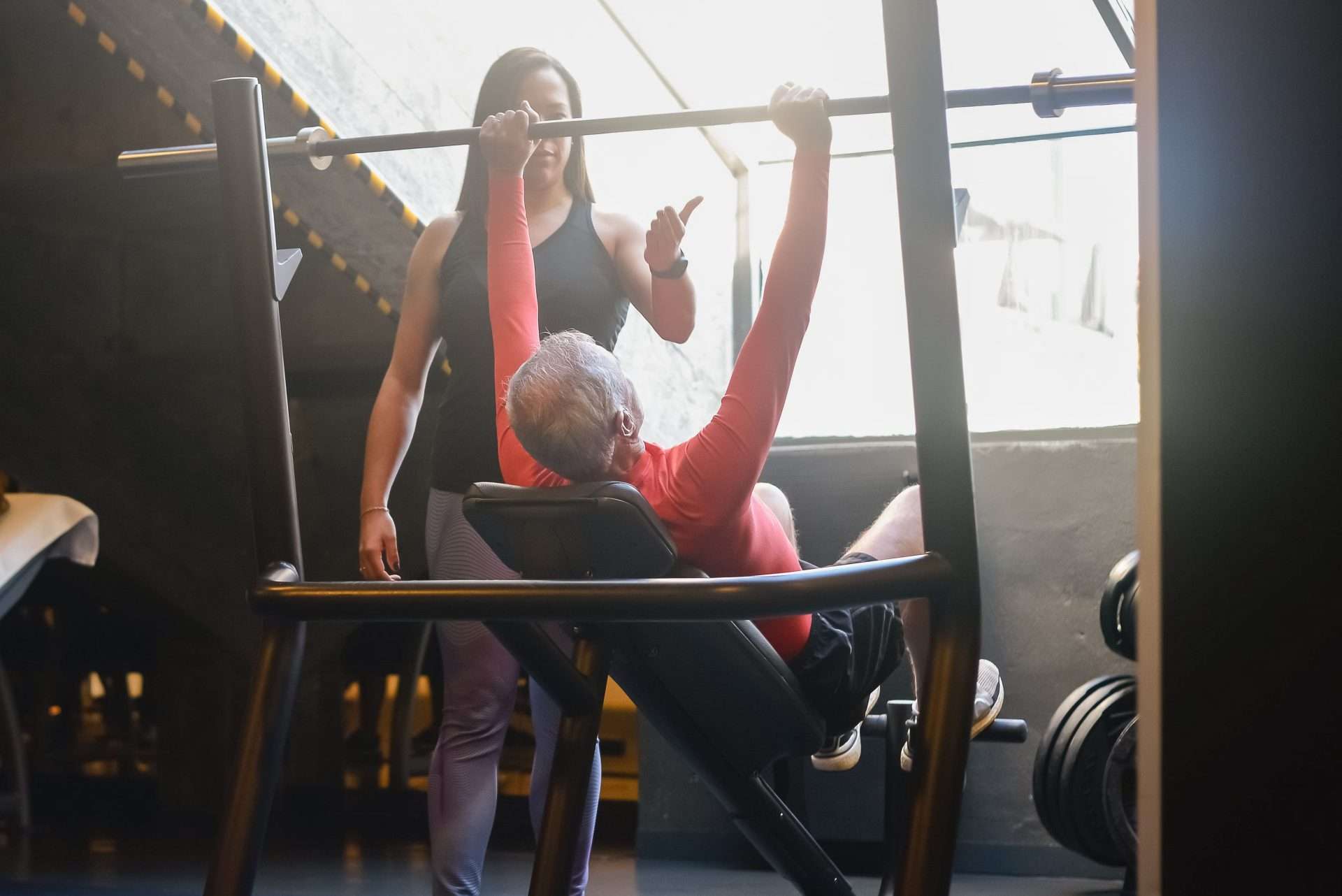 Trainer guiding an older man through a supervised weight lifting set, the strength work regenerative medicine is meant to support.