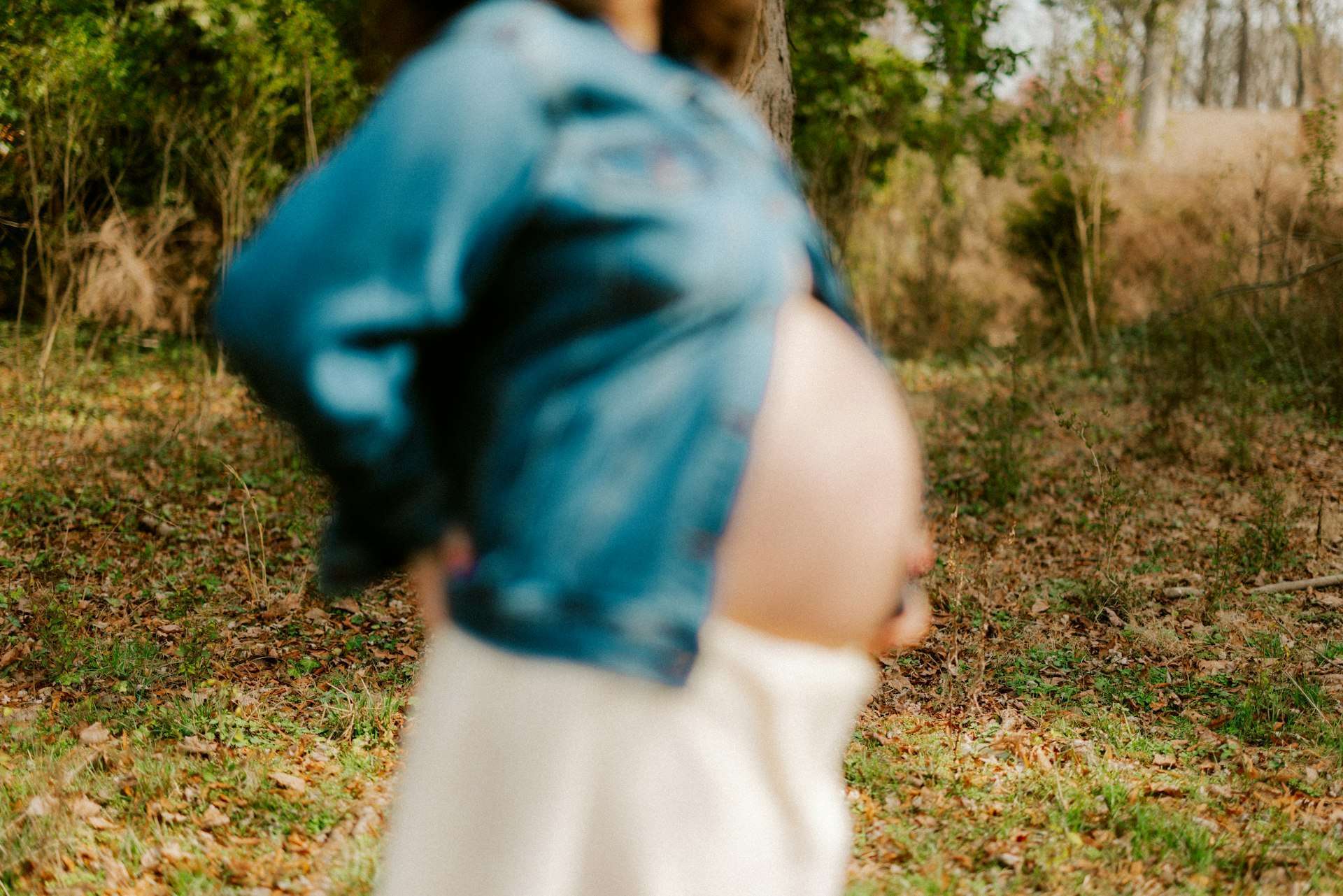Expecting mother walking outdoors in a denim jacket, the gentle daily movement that eases back pain during pregnancy.