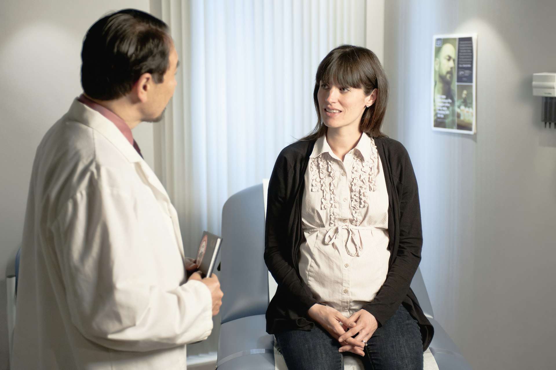 Clinician talking with an expecting patient in a bright waiting room before a prenatal assessment of pregnancy back pain.