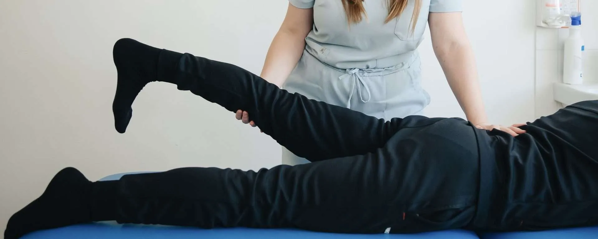 Physiotherapist guiding a fully clothed patient through a controlled leg exercise, the graded loading a hypermobile spine needs