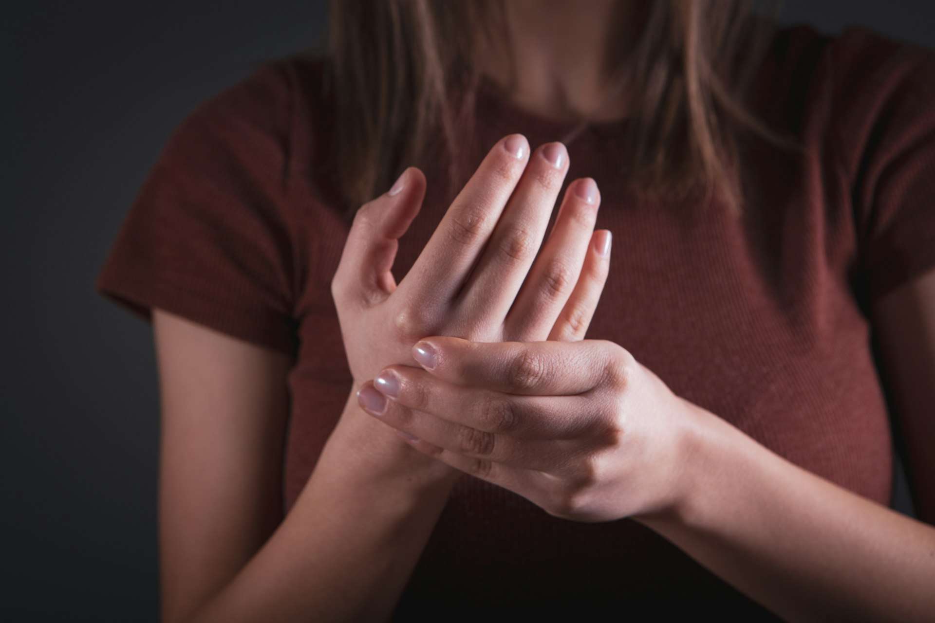 A woman in a red top cradles one hand and wrist with the other, a pose many people link with carpal tunnel syndrome pain.