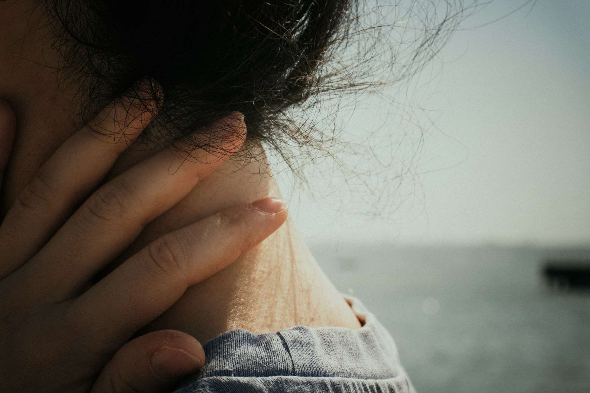 Woman in a gray top presses her fingers to the back of her neck, a common spot for cervical stenosis pain and stiffness