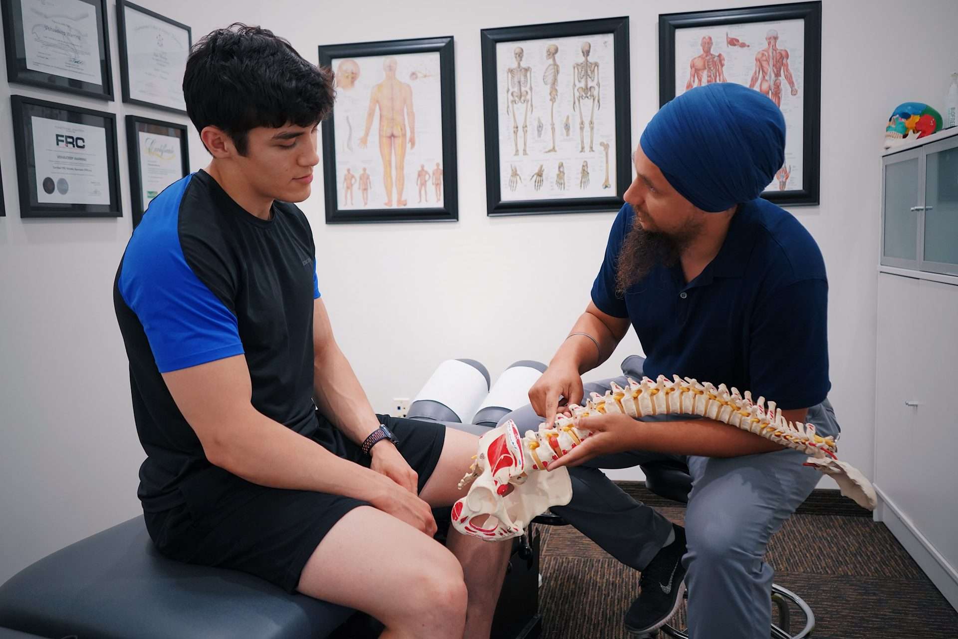 Clinician explaining spinal concerns to a patient with a spine model during a consultation