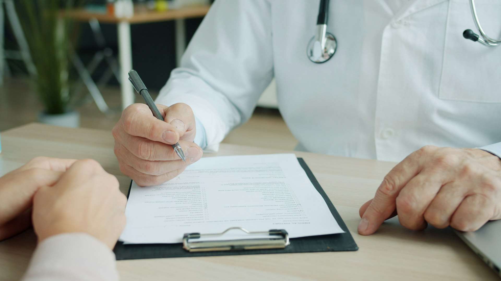 A clinician in a white coat writes on a clipboard form as a patient sits across the desk at a chiropractor near Gaithersburg.