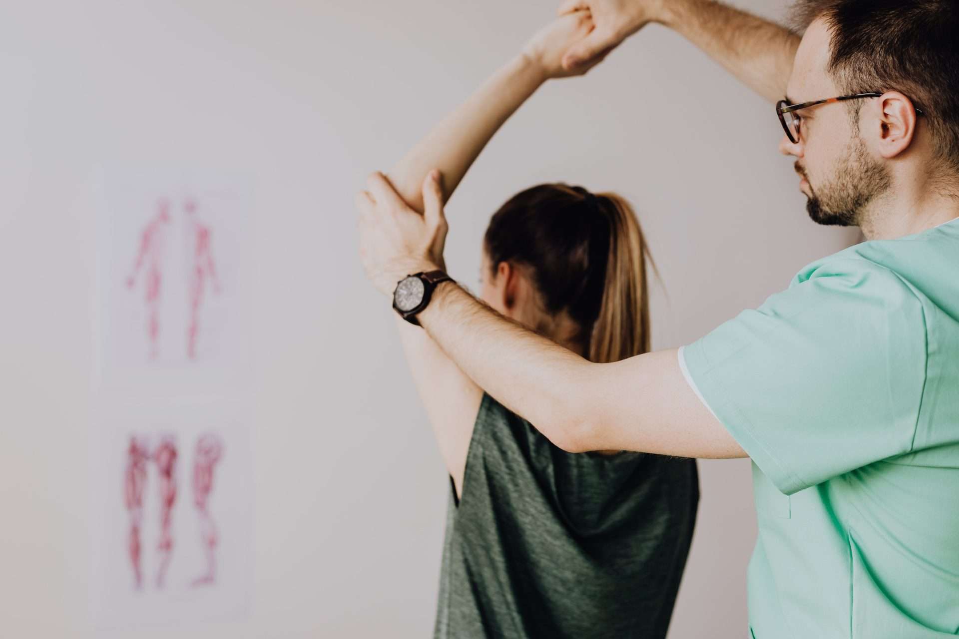 A clinician in green scrubs guides a seated patient's arm overhead, a test that helps trace hand numbness above the wrist.