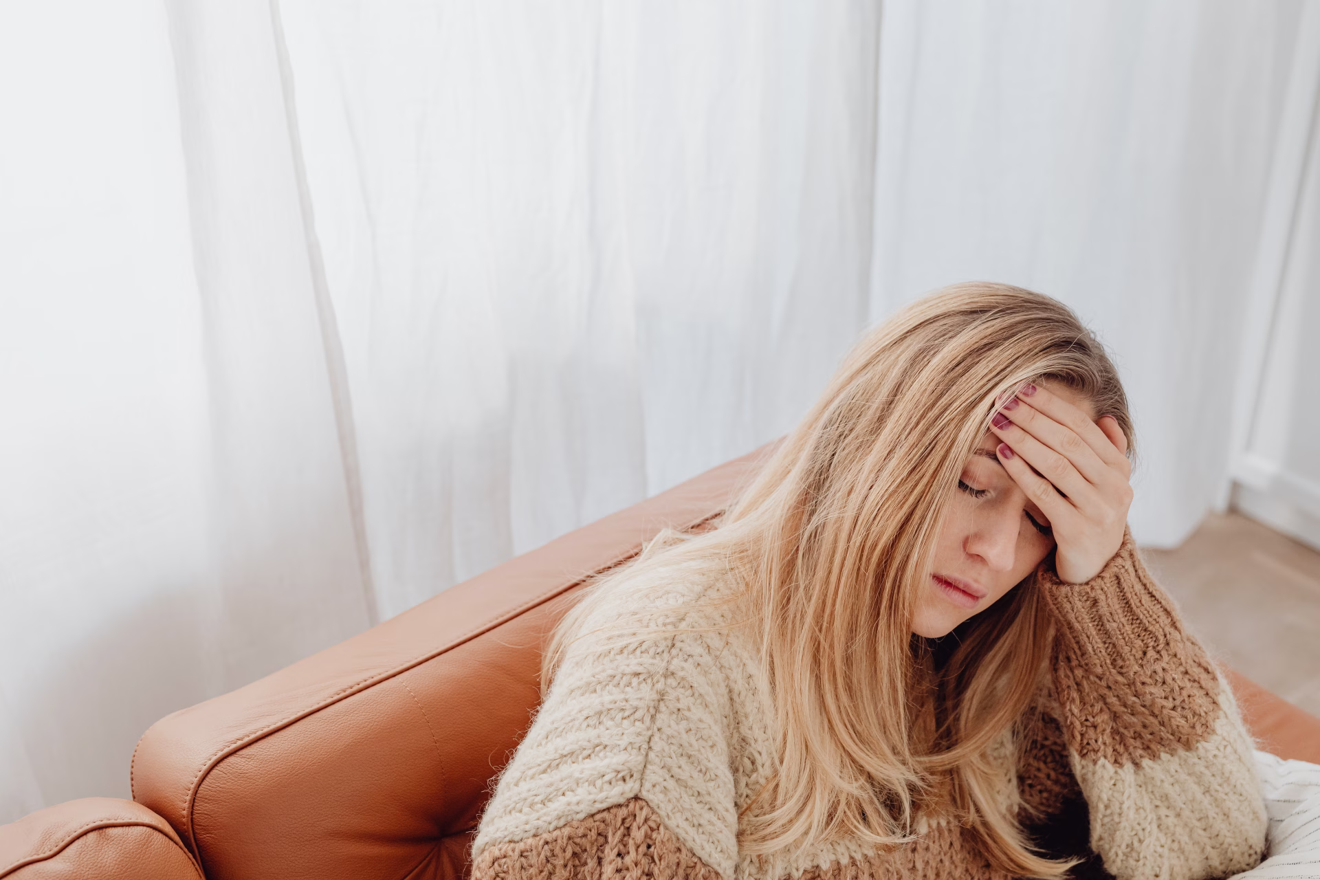 A woman rests on a sofa with her eyes closed and a hand on her forehead, coping with migraines in Bowie beyond head pain.