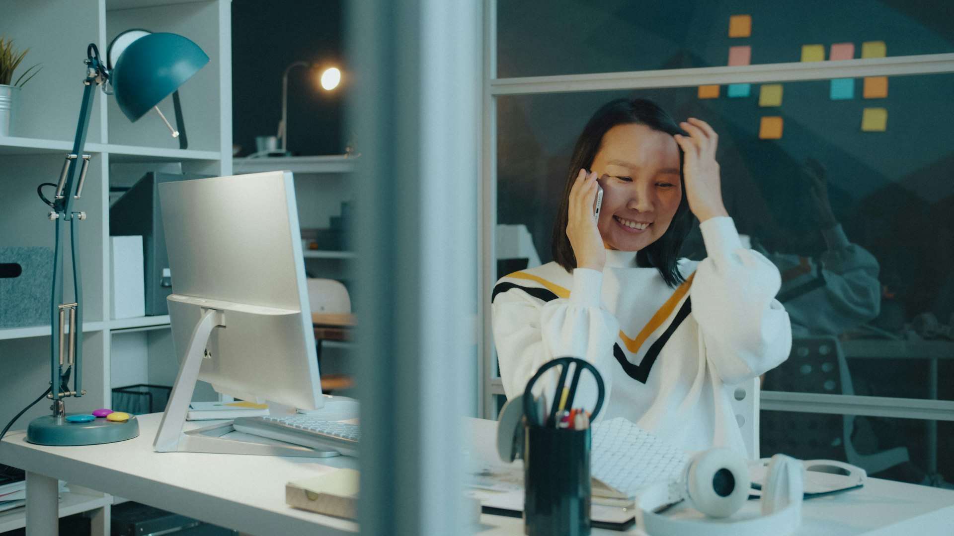 A woman in a white sweater sits upright at a desk and talks on the phone, one easy way to ask about a first neck pain visit.