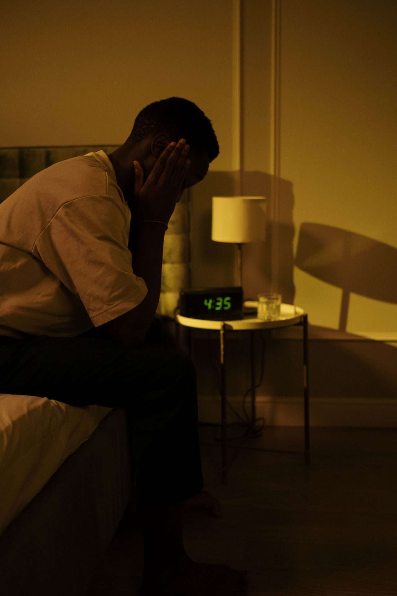 Man sitting on the edge of his bed in a dimly lit bedroom at night