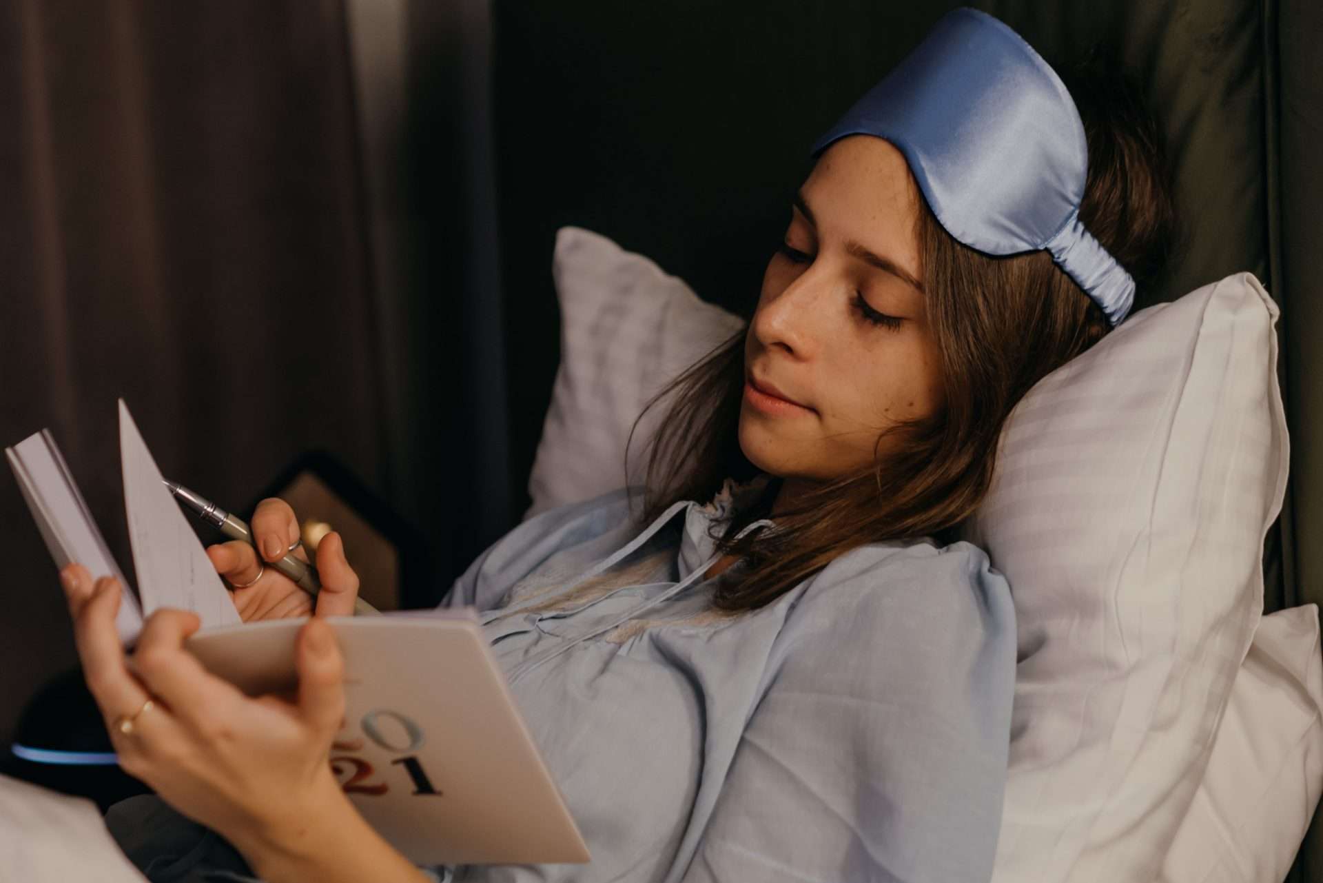 Woman writing in a journal in bed to keep a sleep diary of nighttime patterns and daytime symptoms