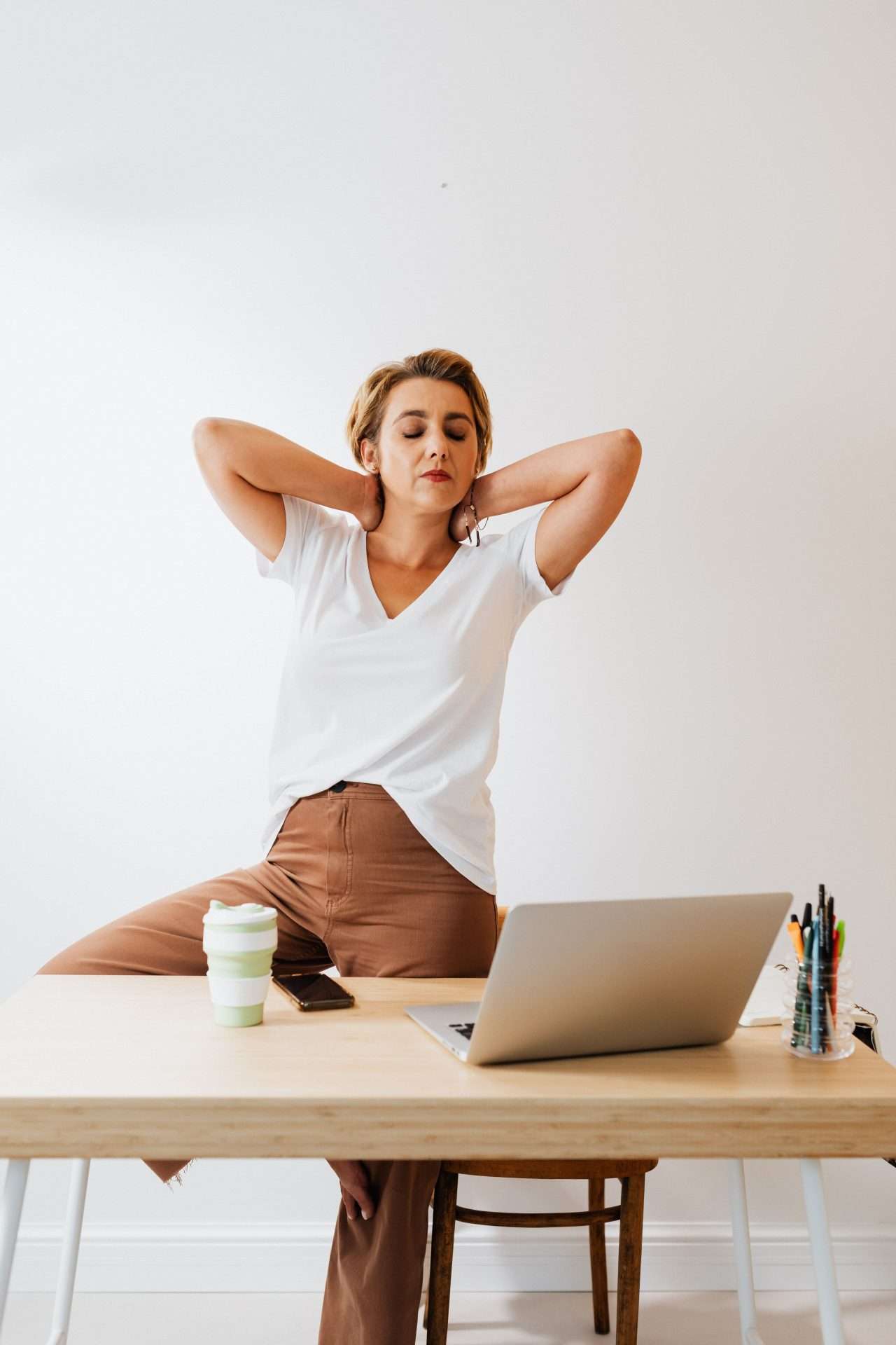 Woman standing beside her desk and laptop to take a brief stretch break during the workday