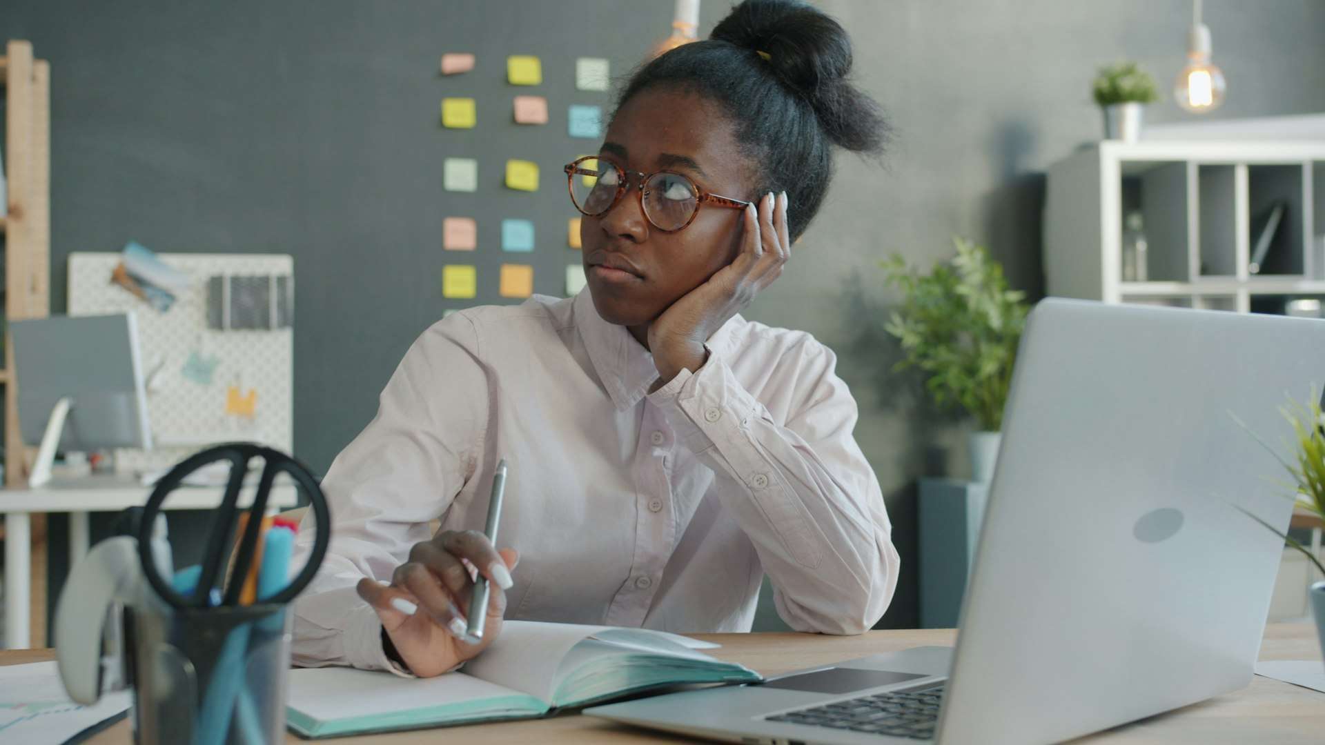 A woman at a laptop desk rests her head on one hand, a sitting posture that can keep a stiff neck sore through the workday.